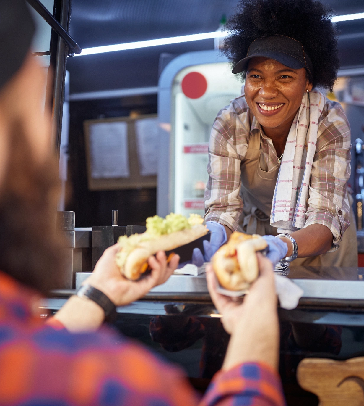 A woman smiles at the camera while holding two hot dogs.