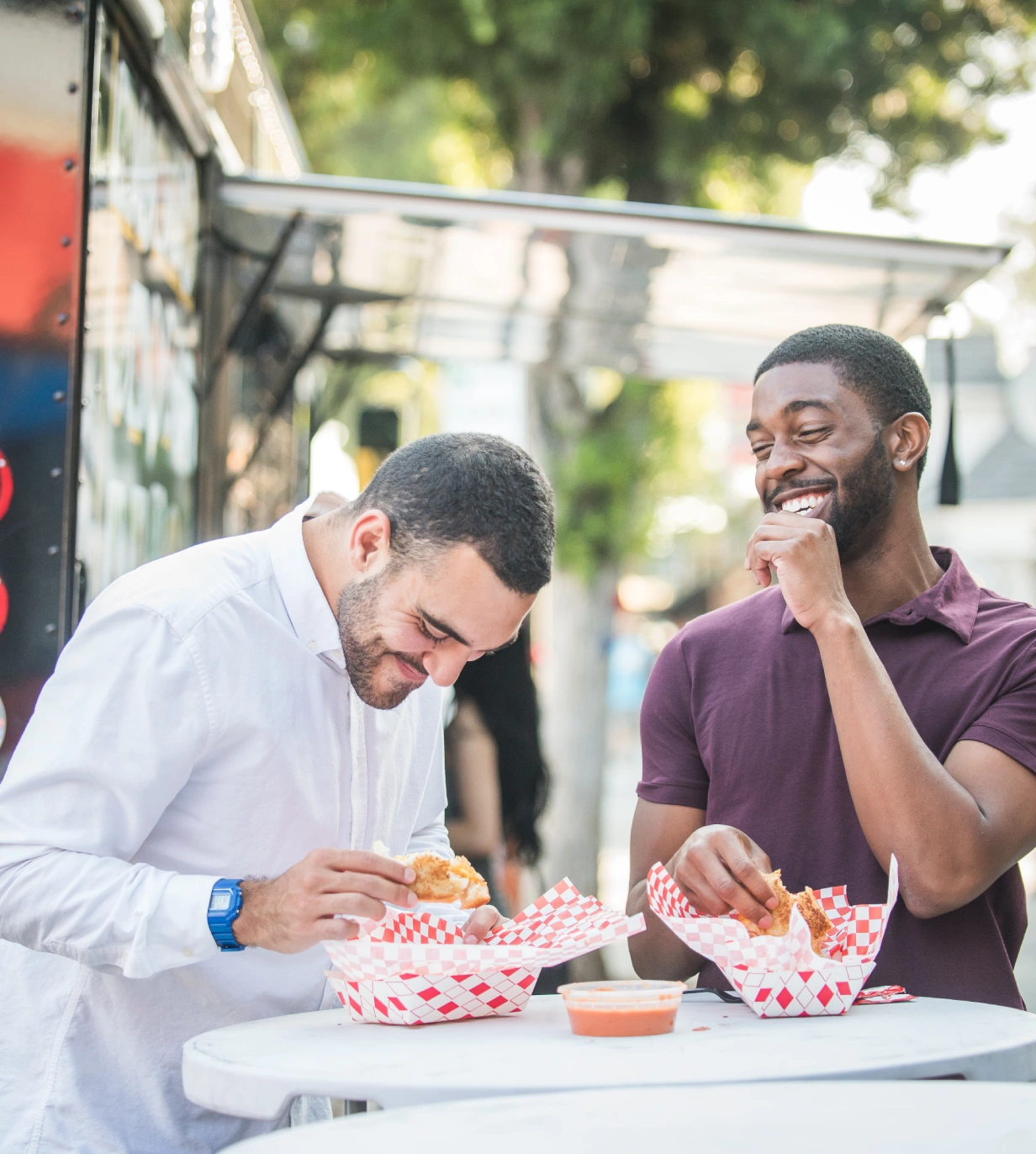 Two men eating food at an outdoor table.