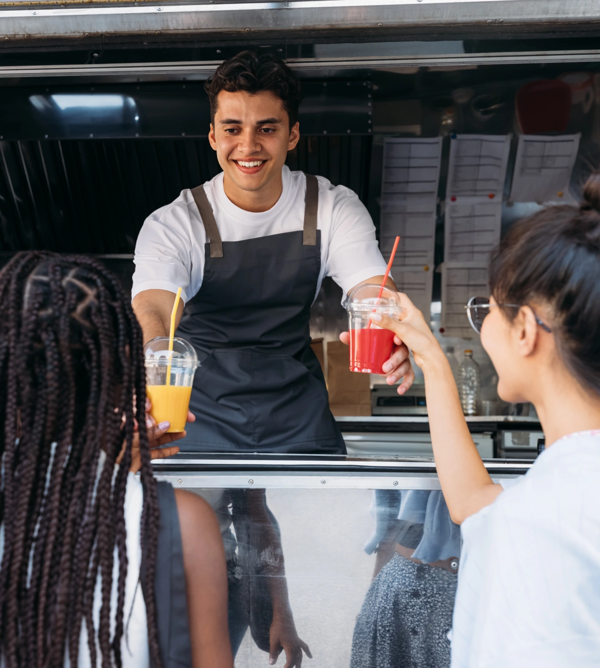 A man serving drinks to people in a food truck.